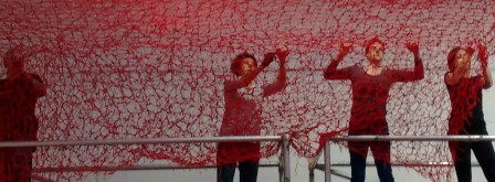 three artists tying red yarn to make a large net